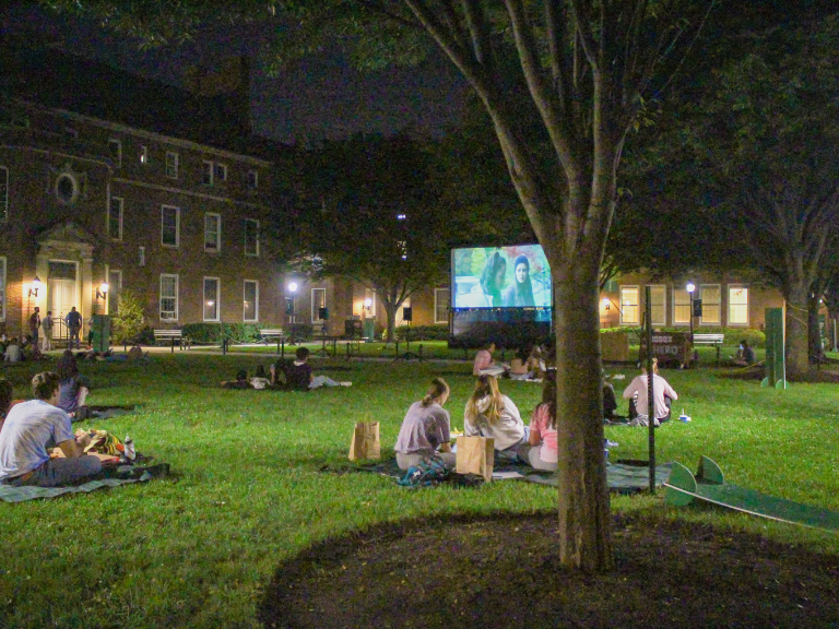 students watching movie together while sitting on grassy area of campus